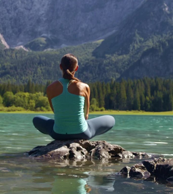 女徒步旅行者坐在岩石上的后视图，欣赏落基山脉之间湖泊的美景
