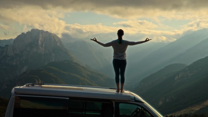 站在屋顶上伸展双臂练习瑜伽手印，欣赏山景美景