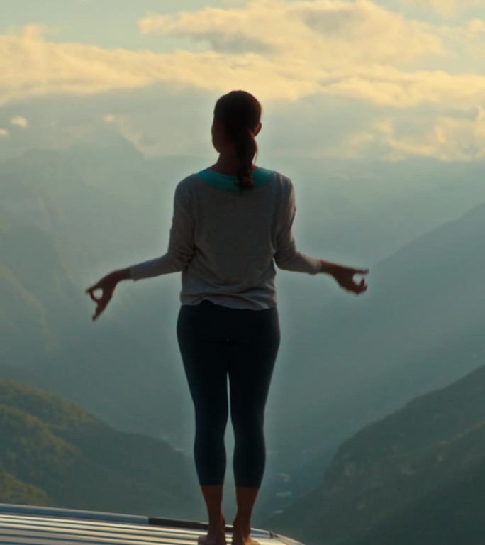 SLO MO女子站在屋顶上，张开双臂拥抱瑜伽，吸收Mangart山的壮丽