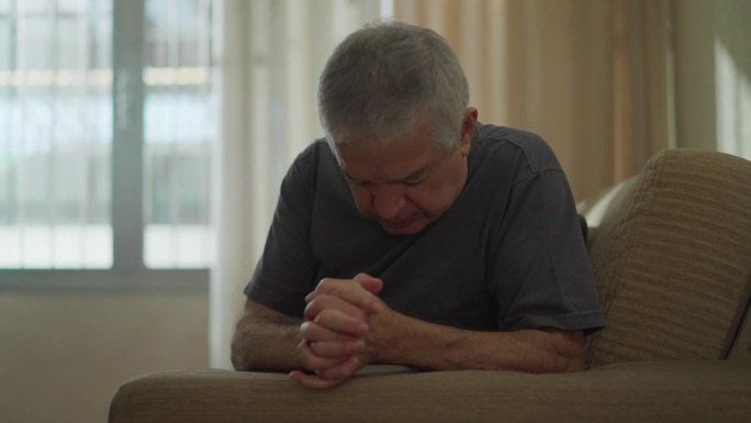 虔诚的老人在家里划十字，年长的白人男性在沙发上祈祷，体现了灵性和希望