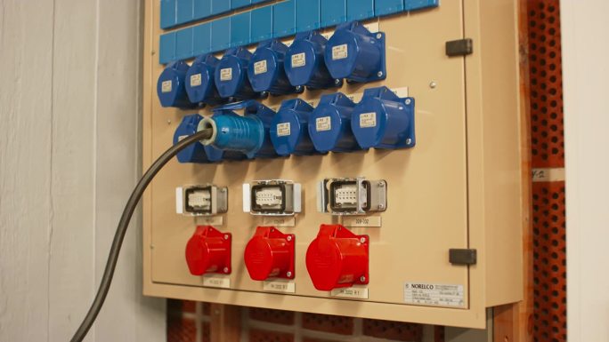 电气面板与蓝色16A和红色32A三相连接器和配电箱。技术人员将16A信号电缆连接到插座上，然后将其取