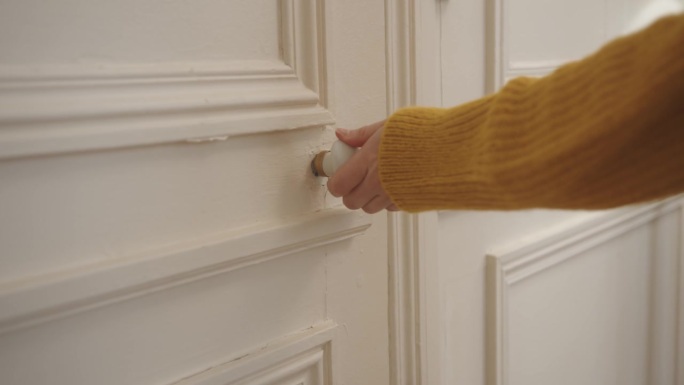 在一所房子里，一位女性用手抓住门把手开门的特写镜头。