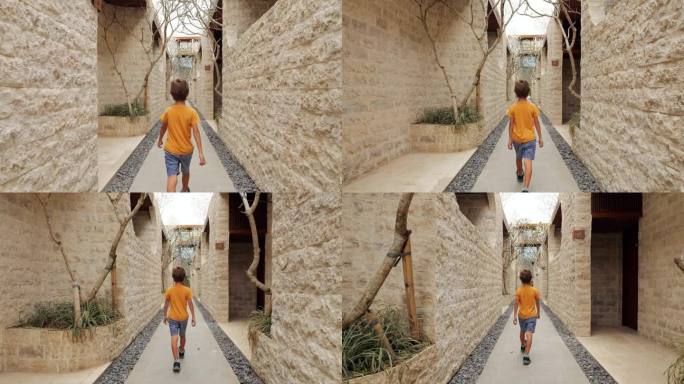 一个小男孩走在一条狭窄的巷子里，巷子的墙是用天然的石头瓷砖砌成的