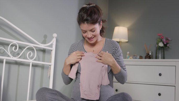 孕妇坐在卧室里整理婴儿衣服