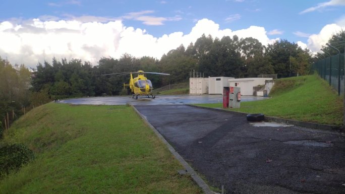 在西班牙加利西亚的圣地亚哥德孔波斯特拉，救援直升机停在直升机停机坪基地，维修大楼在一天的白云后面