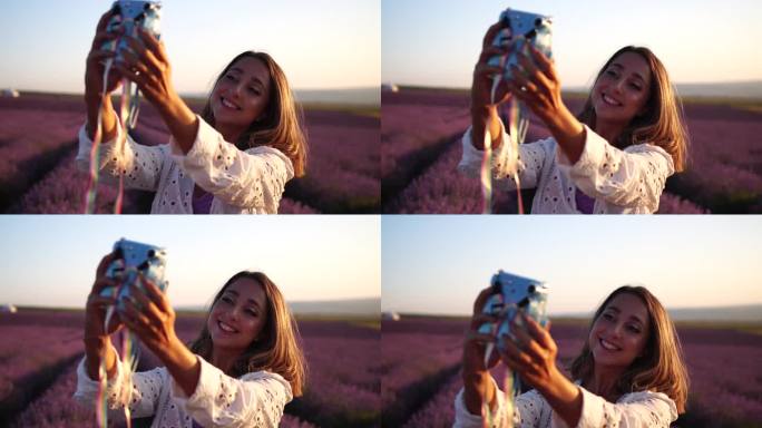 阳光明媚的日子里，在薰衣草地里，一个微笑的快乐女人拿着相机拍照。年轻女子用蓝色的即时相机拍摄——时髦