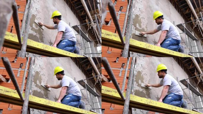 一名蓝领工人跪在脚手架上，在建筑工地给墙浇水泥