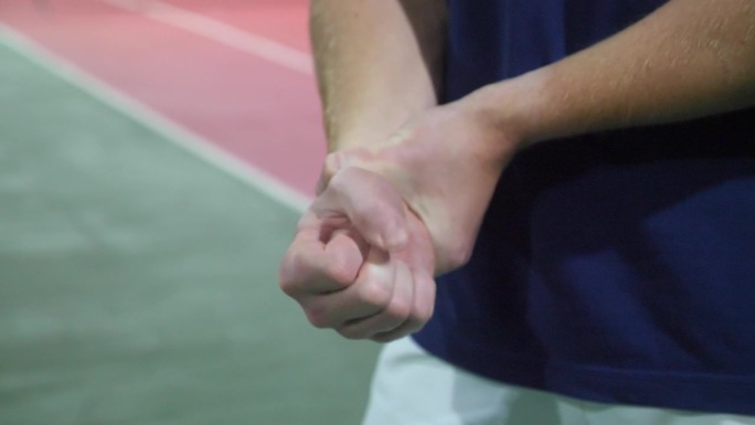 一个年轻人在硬地场上打网球时手腕受了伤。
