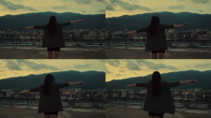 年轻的黑发女孩双手张开，在山景的屋顶上跳舞