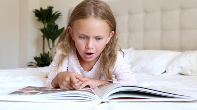 情绪激动的孩子在床上读有趣的书。小孩子喜欢阅读新的事实指手画脚。培养孩子的幻想。想象的世界童话。幼儿