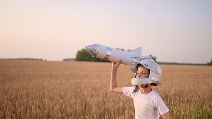 可爱的小男孩，戴着头盔的少年，飞行员，宇航员，带着玩具火箭在日落的田野里奔跑，夏日的大自然。孩子大梦