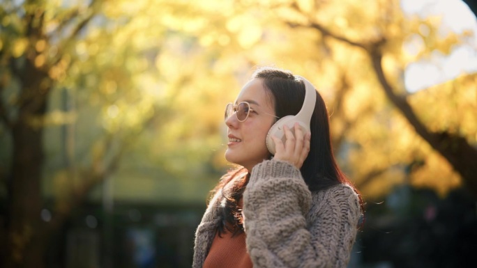 一个欢快的亚洲孕妇周末在公园边散步边听音乐的特写。