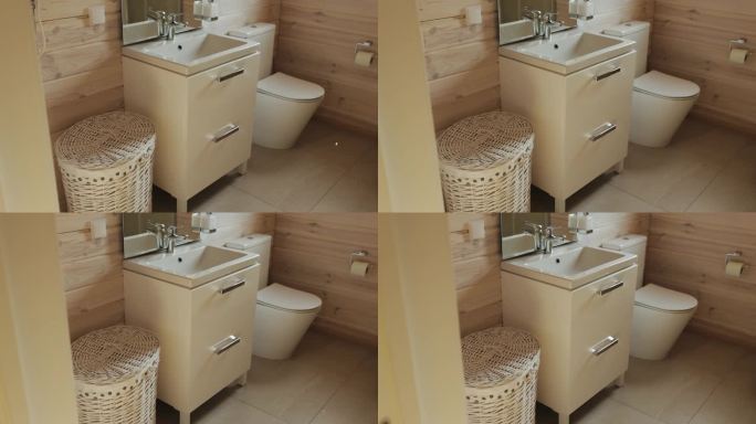 小浴室的内部，有木墙、镜子、水槽、马桶和柳条篮子，用来放脏衣服。