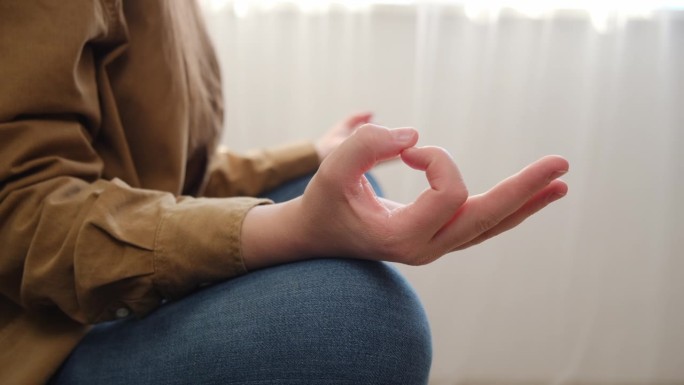 安静的女人坐在莲座和冥想，坐在家里的沙发上练习瑜伽，手的手指观看，平静的女性控制情绪，没有压力，健康