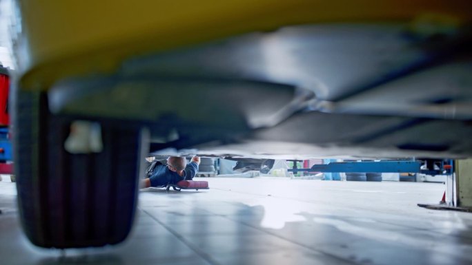 男机械师在修理厂的汽车下工作