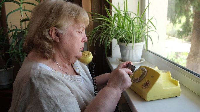 一位老妇人在家里用圆盘电话拨了一个号码