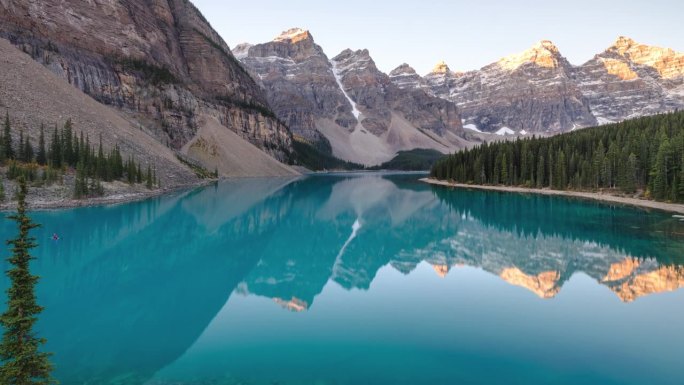 日出延时拍摄在清晰，原始的高山湖泊在加拿大落基山脉。日出照亮了群山。一对夫妇在蓝色的湖面上划船。