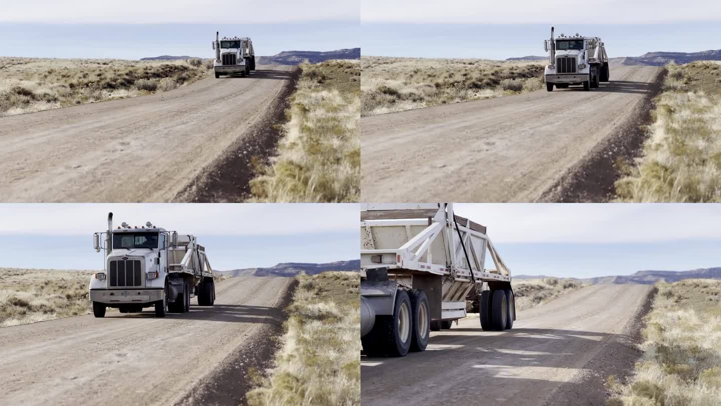 在一个阳光明媚的冬日，手持拍摄的一辆白色半挂车在犹他州沙漠的土路上拖着一辆自卸拖车