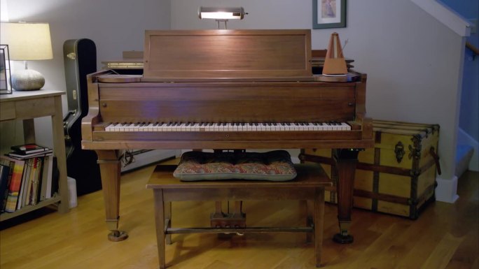 客厅里放着一架老式木制钢琴，右边摆着一个以每分钟60拍摇摆的古董机械节拍器，后面摆着一个吉他盒和一个