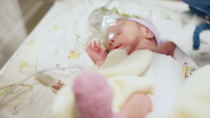 刚出生一天的婴儿在重症监护室的医疗孵化器里。孩子手的微距照片。新生儿救助概念。