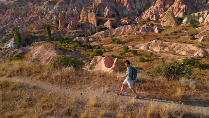 一个游客家庭徒步穿越卡帕多西亚戈雷梅附近的红色或粉红色山谷。以暖色调绘制的景观展示了独特的地质构造和