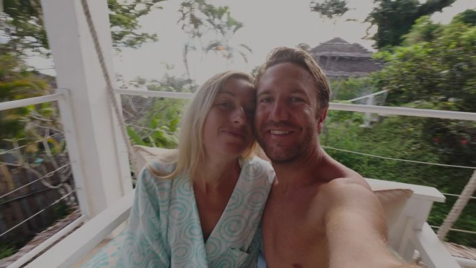 度假的年轻夫妇在酒店房间的吊椅上摇摆自拍，看到了热带雨林的景色