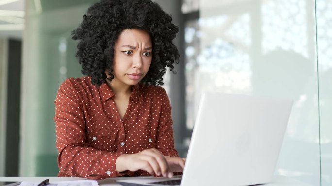 沮丧的年轻非裔美国女性在办公室抱怨笔记本电脑上的软件性能差。