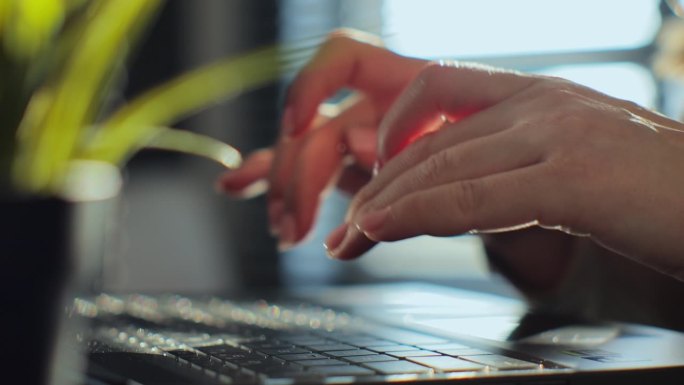 女人的手在笔记本电脑上打字，笔记本电脑键盘坐在家里的办公桌上工作。技术概念，近景侧视图。在线教育，应