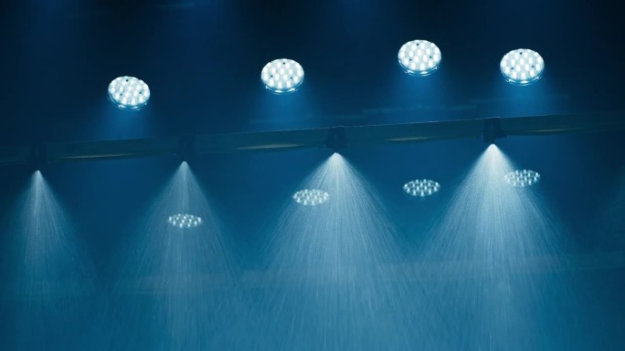 电影制片厂的特效雨机，天花板上挂满了电影灯。清晰可见的带有led音乐视频灯的喷头正从后面照亮喷雾。