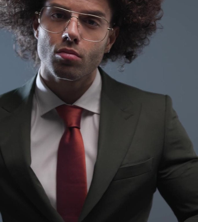 垂直视频酷时尚的男人与眼镜看向一边和关闭黑色西装在灰色背景前