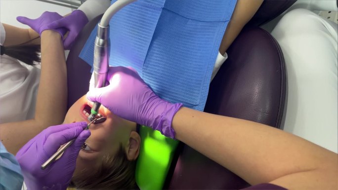 一位戴着医用口罩和紫色橡胶手套的牙医给一个蹒跚学步的小男孩戴上了印章。牙科治疗、检查、小儿牙科。专业