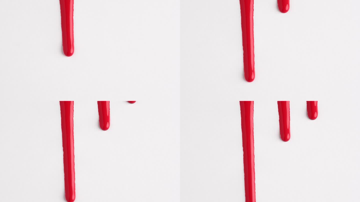 血红色的液体滴在白色的表面上流动。深红色的油漆滴在白色墙上的微距镜头与复制空间。生产特写。慢动作，抽