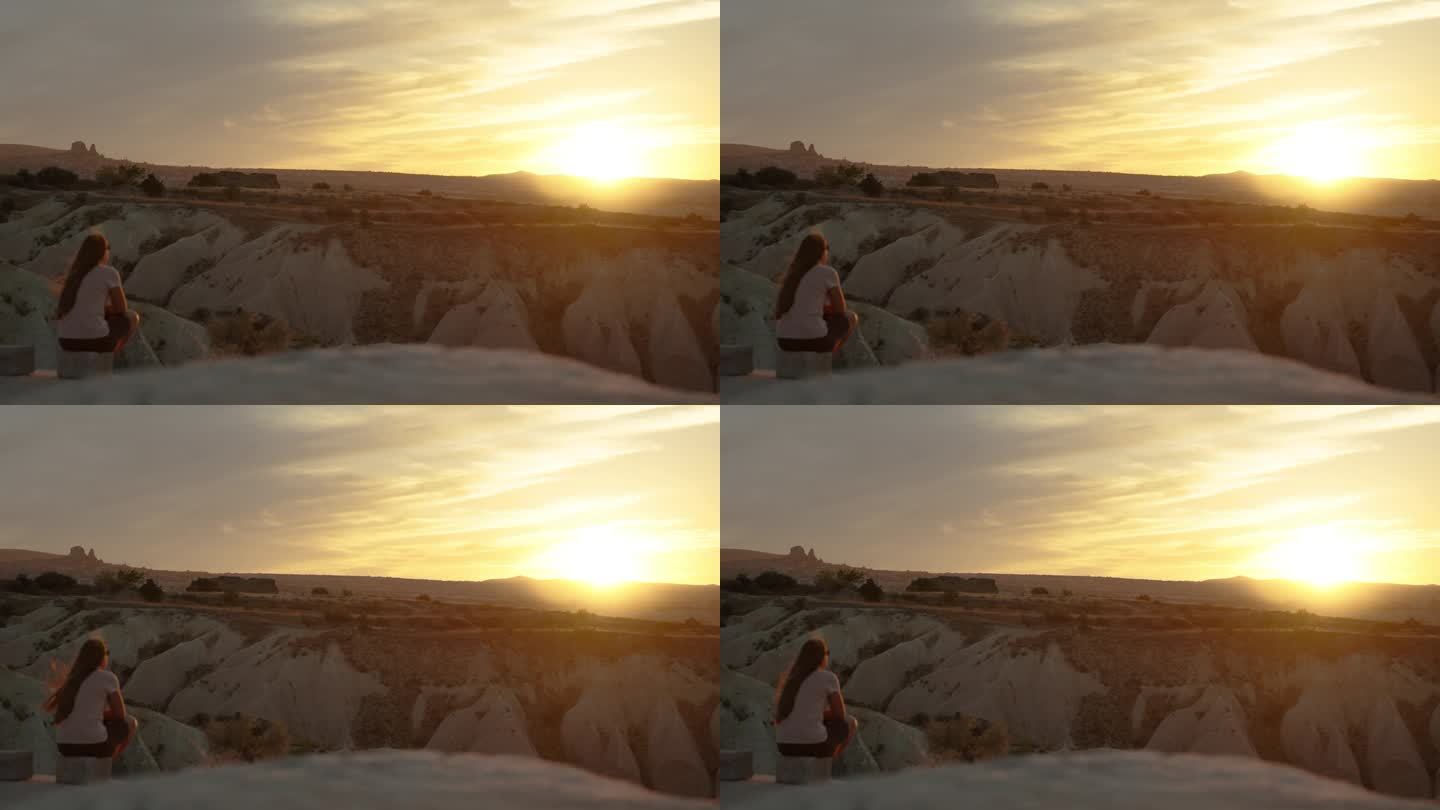 一个年轻的女子坐在山崖边，欣赏着夕阳，表达着宁静和孤独，只有风轻轻地拨弄着她的头发。