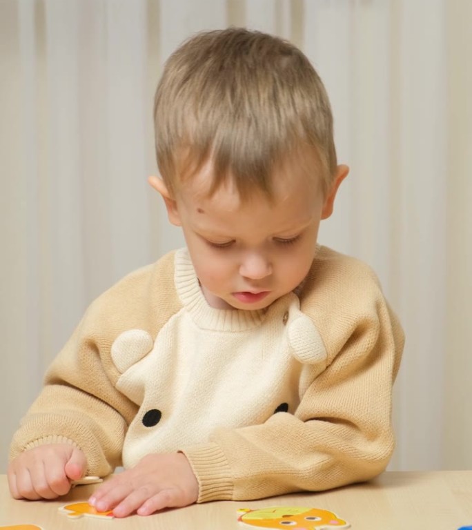 可爱的两岁男孩坐在桌旁拼拼图。逻辑和运动技能的发展，垂直射击