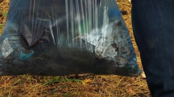 一位女环保主义者在森林里收集垃圾。一位手里拿着蓝色垃圾袋的妇女在森林里收集塑料垃圾。一位妇女拯救了被