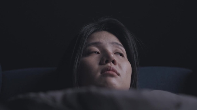 美丽的亚洲女人躺在家里客厅的沙发上，黑暗中有抑郁和悲伤，保健和医疗的概念