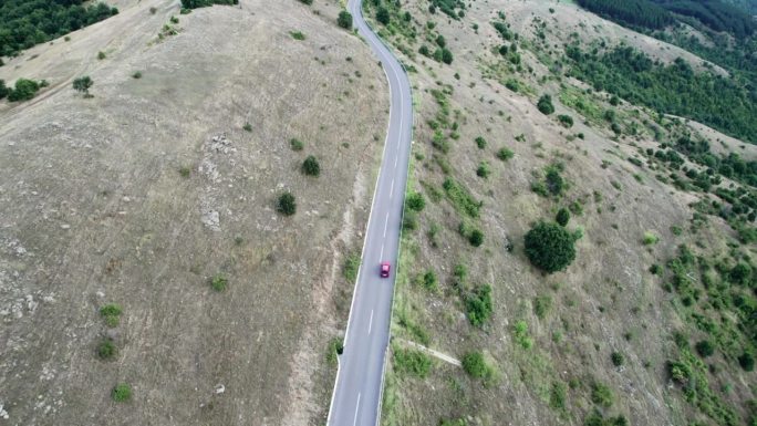 红色赛车在弯弯曲曲的山地乡村公路上疾驰，高速鸟瞰