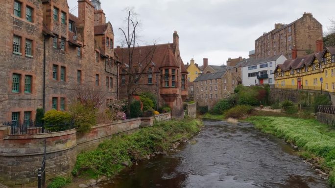 慢动作的平底锅穿过流动的河流，在苏格兰爱丁堡高大的老棕色砖建筑之间的青苔岸边冒着泡泡