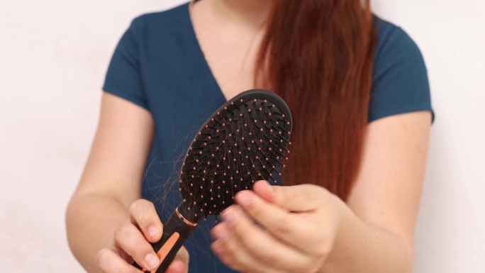 脱发。不可识别的女人用按摩梳梳头发，并立即去除梳子上大量掉落的头发。头发和头皮护理产品。缺乏微量元素