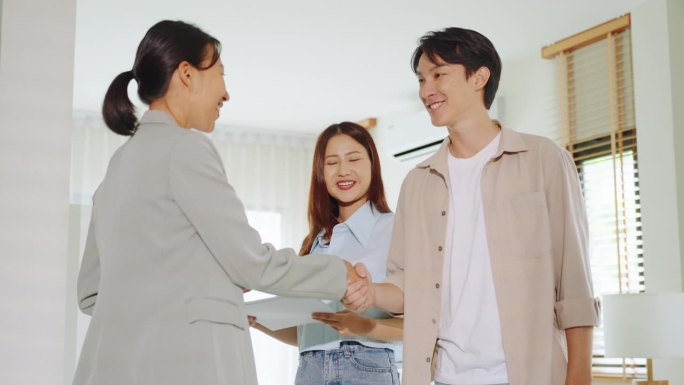 年轻的亚洲已婚夫妇与房地产经纪人握手生意成交协议买新房成功