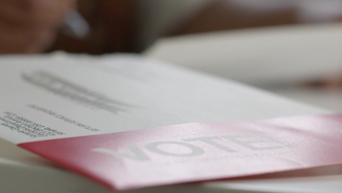 一位黑人妇女在家中填写总统、参议院、国会或地方选举的邮寄选票，手持“投票!”的慢动作信封