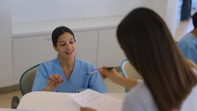 快乐的护士在医院的挂号台让一位女病人填写表格