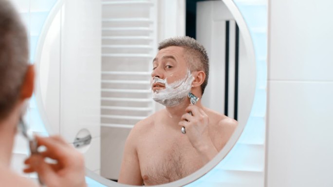 剃刀剃男人的脸。白人男子用剃须刀刮脸。剪掉脸上的胡茬。没刮胡子的男人在剪胡子