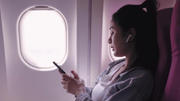 目前，乘坐飞机旅行的亚洲女性正愉快地戴着耳机听音乐，轻声哼唱。能唤起快乐和放松