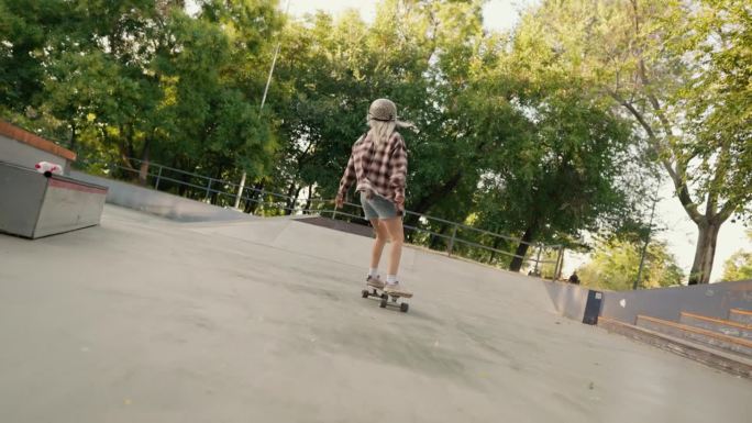 夏天，一个金发女孩在滑板公园的混凝土地板上疾驰而过。一个穿着格子衬衫和牛仔短裤的金发女孩在滑板公园里