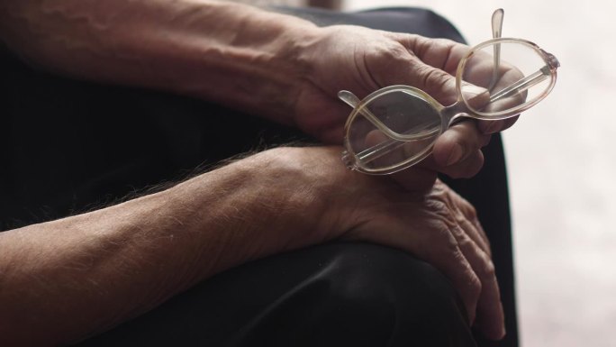 一位视力不佳的老人手里拿着一副老式眼镜。老年人的日常生活。老年视力减退家里真正的养老金领取者