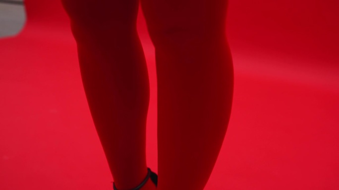 一个穿着红色紧身衣的女孩的腿，红色的背景，红色的毛衣。艺伎在摄影棚里摆姿势
