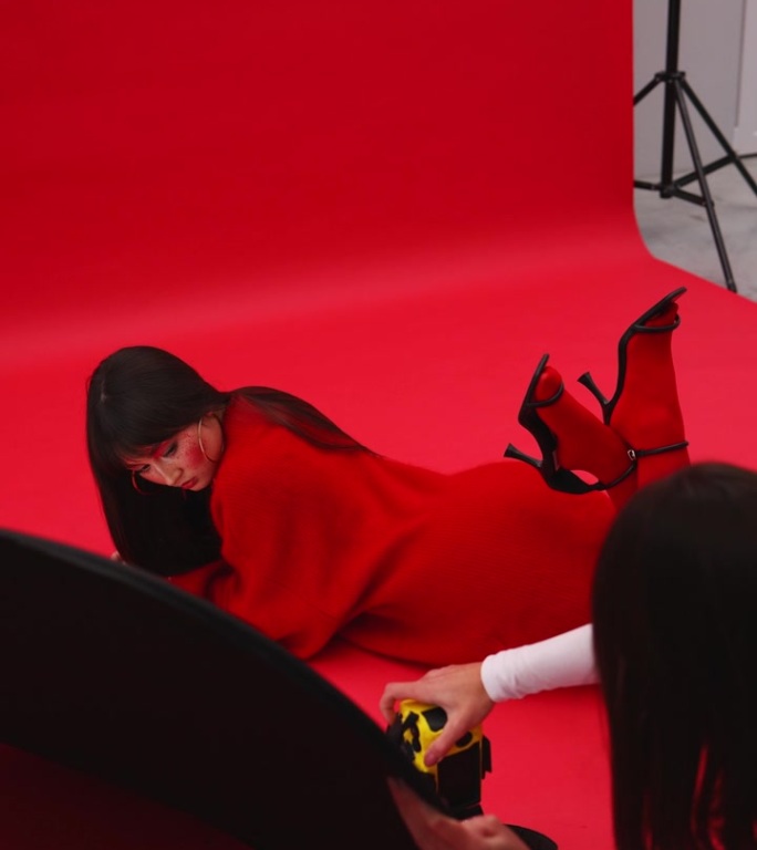 一名女摄影师拍摄了一名亚洲模特，她身穿红色毛衣和连裤袜，趴在红色背景的地板上。艺妓穿着红色的衣服。垂