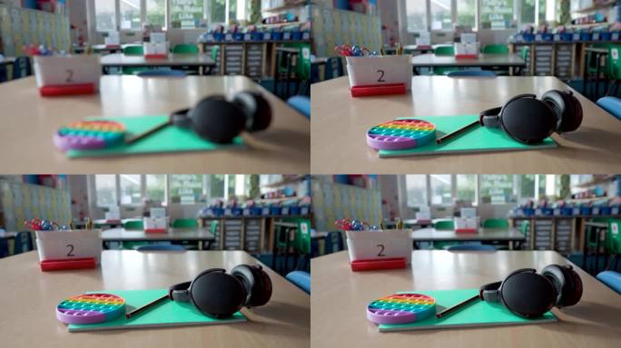 在空荡荡的学校教室里，桌子上放着护耳器、耳机和烦躁玩具等帮助自闭症儿童的工具