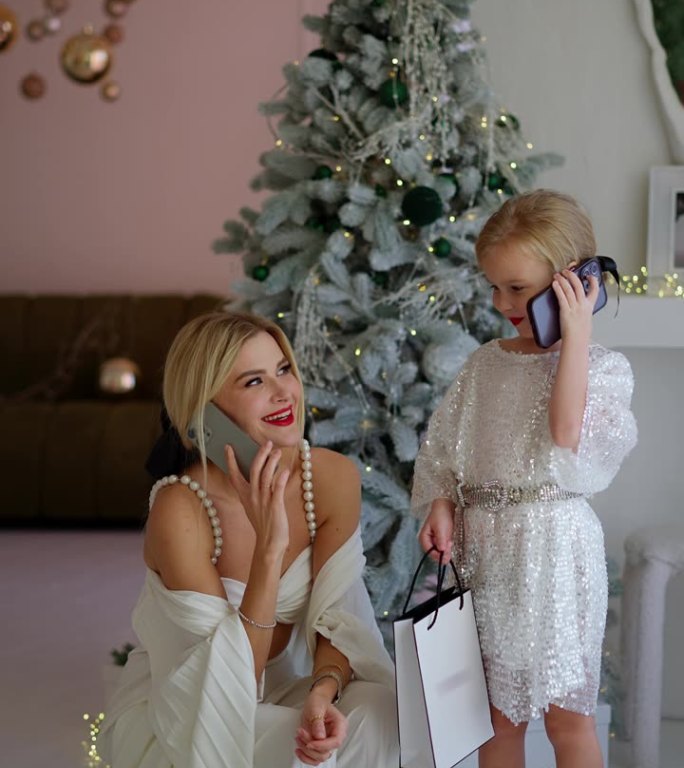 妈妈和女儿在圣诞树旁玩得很开心，用手机聊天